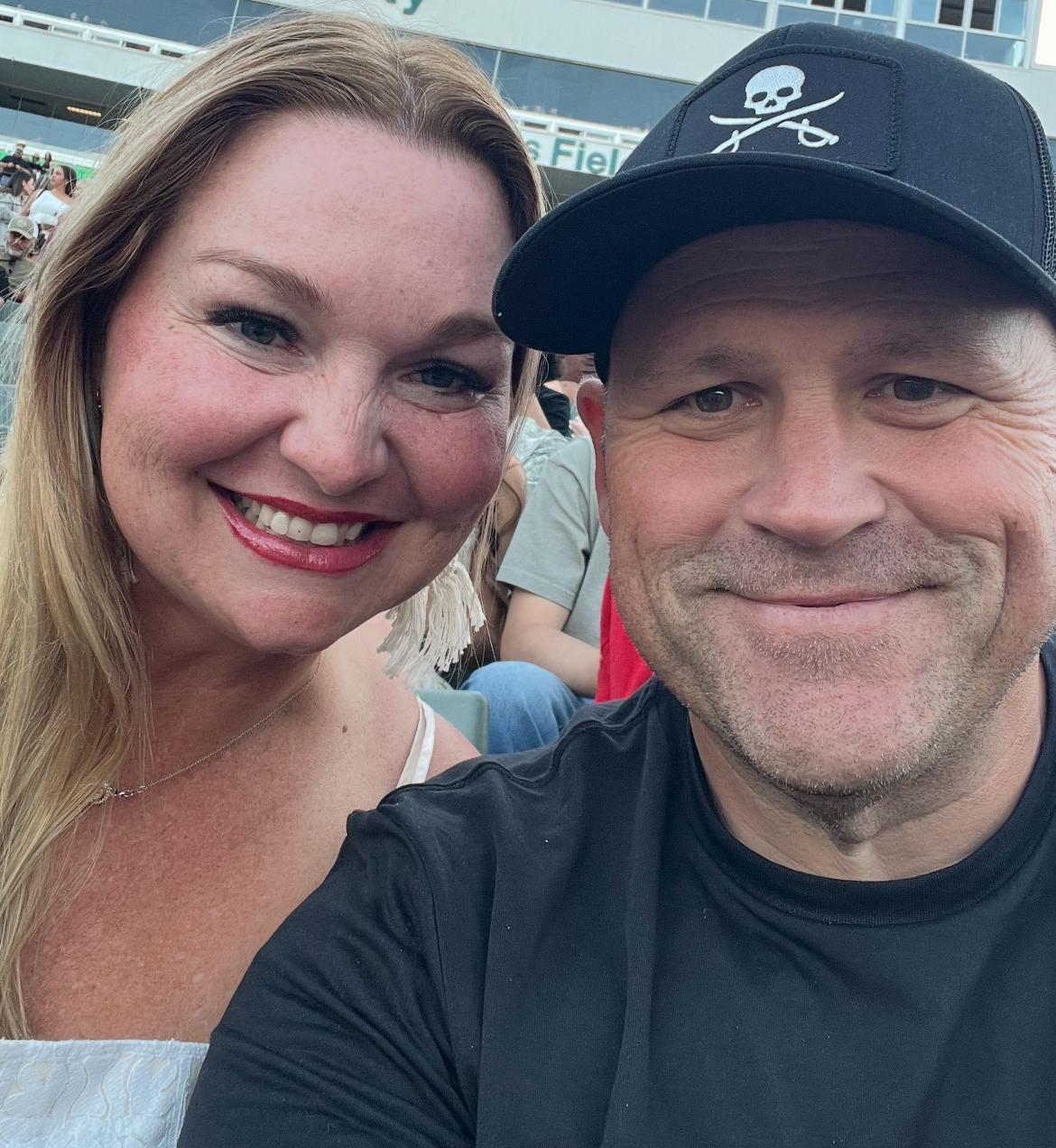 Smiling man and woman taking a selfie at an outdoor event.